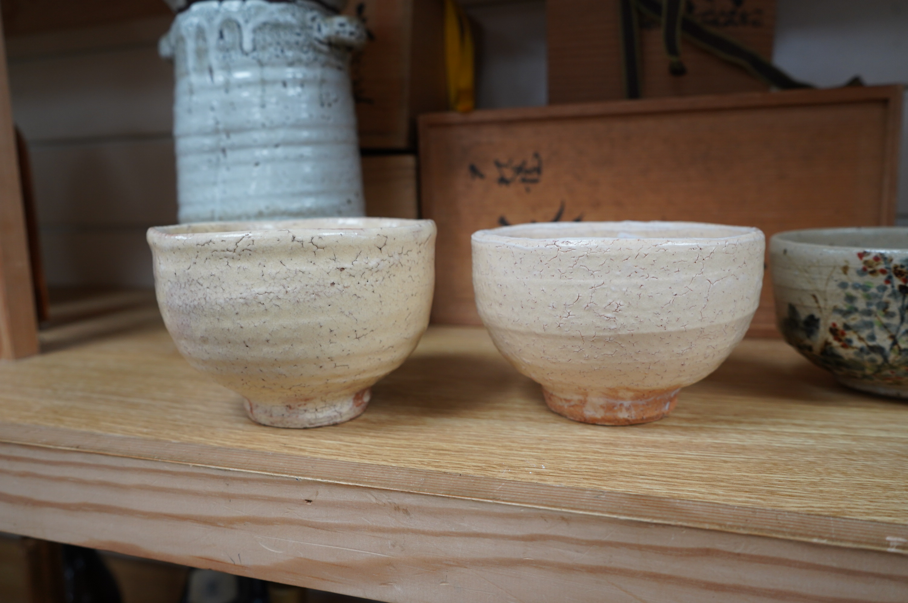 Japanese studio pottery comprising a Nishiyama (Contemporary Japanese School) tea bowl in the Yashichida style decorated with flowers (fitted box), a near pair of Japanese studio pottery cream ground raku bowls (fitted b